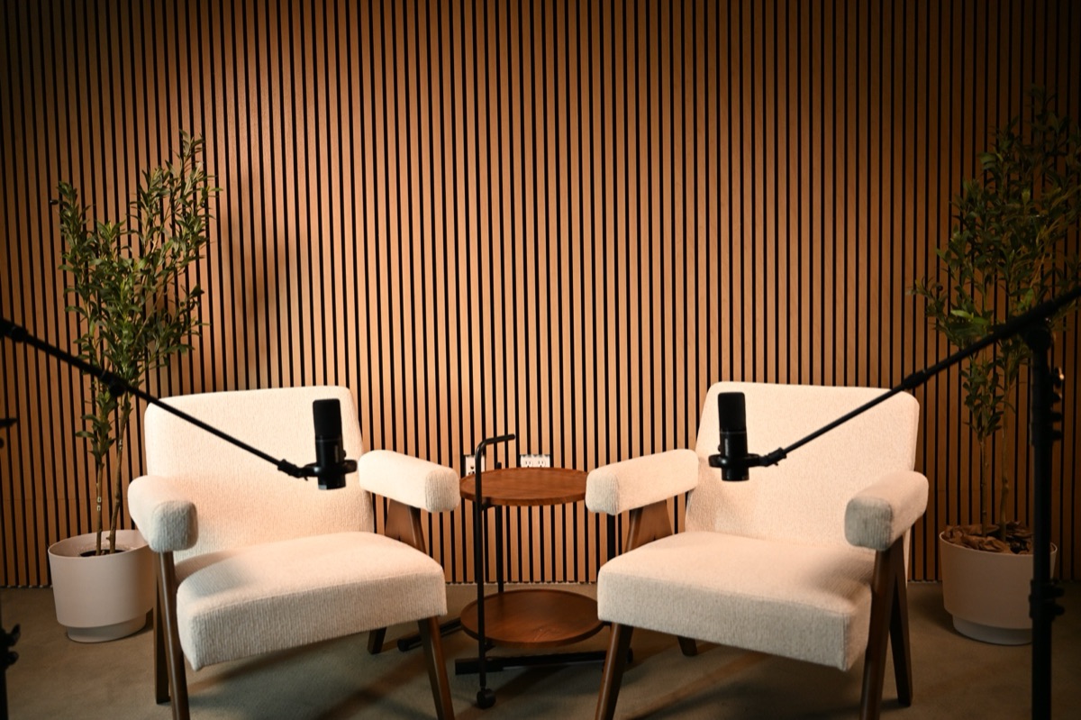 Two boucle armchairs and microphone booms in front of a wood-slat backdrop at the Axeom studio in Addison, TX.